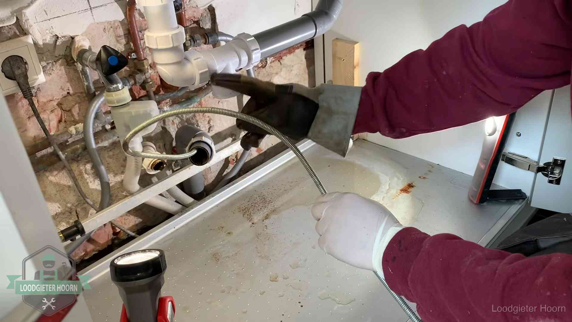 Ontstoppingsveer gaat in een geopende sifonaansluiting onder het aanrecht in Hoorn