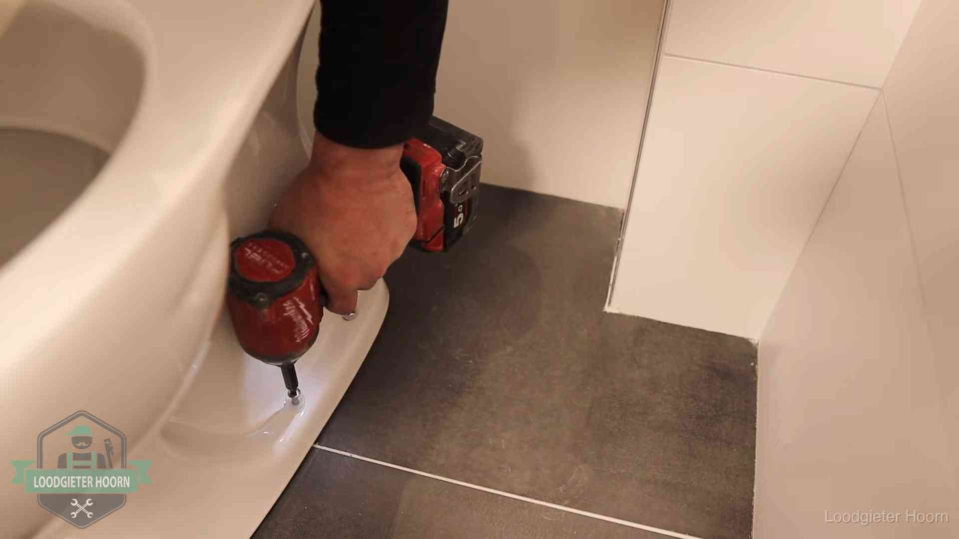 Loodgieter zet de voet van een wc-pot vast op de tegelvloer in Hoorn